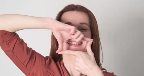 Young woman creates rectangle shape with her hands. Shows his braces, focuses on Stock Footage 240003802