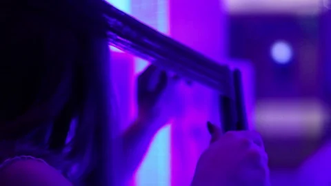 Young woman Curling her hair on tongs, doing her hair styling in neon light room Stock Footage