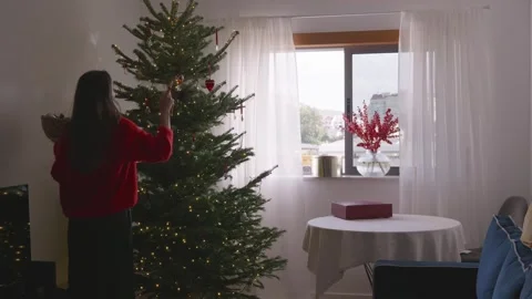 Young woman dancing and decorating Christmas tree in cozy bright living room, 4K Stock Footage 324923937