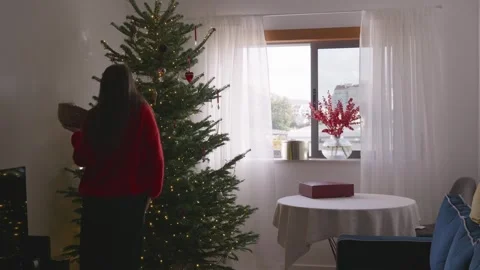 Young woman dancing and decorating Christmas tree in cozy bright living room, 4K Stock Footage 324923966