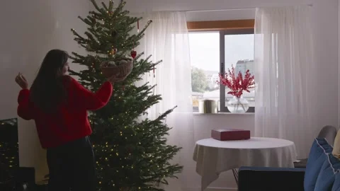 Young woman dancing and decorating Christmas tree in cozy bright living room, 4K Stock Footage 324923980