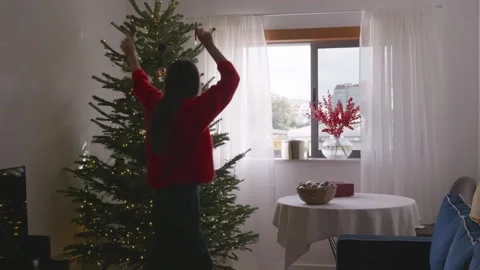Young woman dancing and decorating Christmas tree in cozy bright living room, 4K Stock Footage 324924070