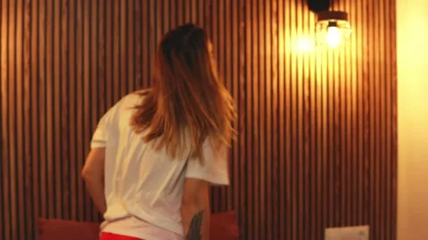 Young woman dancing energetically on bed, wearing white t-shirt and red sho.. Vidéo 303915134