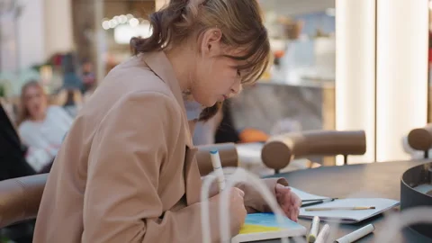 Young woman in deep focus drafting small artwork with markers at mall cafe table Video stock 322906374