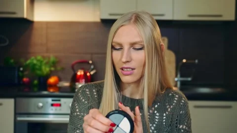 Young woman demonstrating makeup compact in kitchen setting Stock Footage 340274007