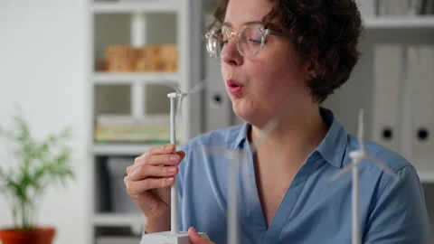 Young woman demonstrating a small wind turbine model in a well-lit office en Stock Footage 323717296