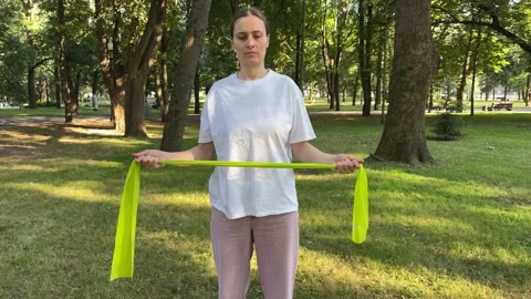 Young woman doing arm exercises with green resistance band in park Stock Footage 340149063