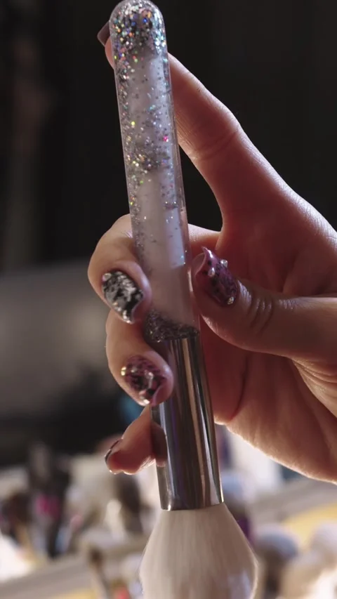 Young woman doing make up at the backstage - holding a brush with glitter in the Stock Footage 328075688