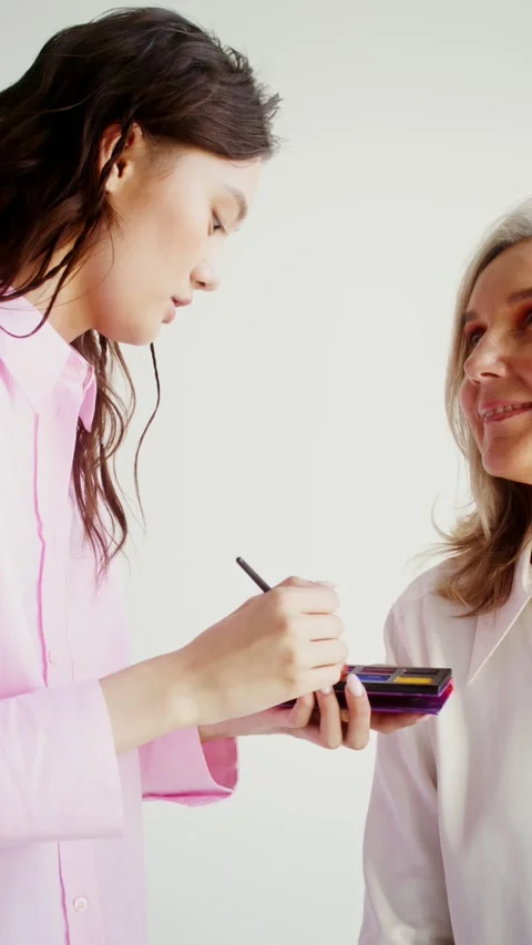 Young woman doing makeup of an older model - Care. Stock Footage 323943489