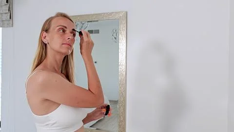Young woman doing makeup while looking in the mirror Fotos de archivo