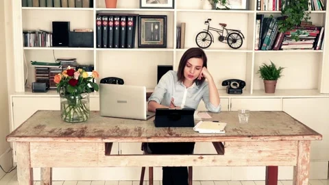 Young woman doing notes and comparing data on laptop and tablet by table at home Stock Footage 103375004