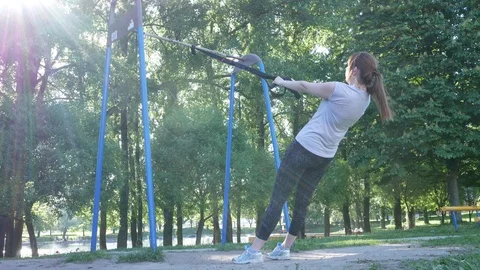 Young woman doing pull-ups with fitness loops in a park. 4K slow mo footage Stock Footage 99509577