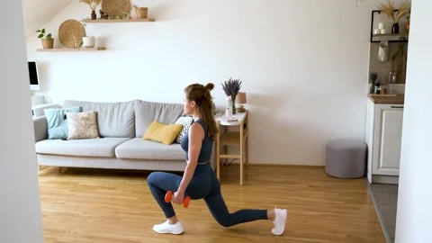 Young woman doing squat exercise with dumbbells during home workout Stock Footage 310372923