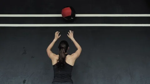 Young woman doing squats while throwing medicine ball up against wall in gym 스톡 동영상 109988506