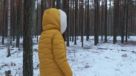 A young woman in a down jacket is walking through a winter forest among trees. A Stock Footage 129382486