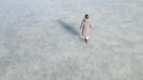 Young woman in a down jacket walking on frozen ice aerial view. Stock Footage 219522517