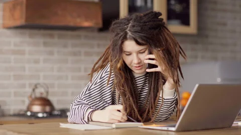 Young woman with dreadlocks talking on cell phone while working from home Stock Footage 165696261