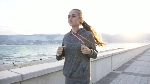 Young woman dressed in hoodie jogging in the city at seafront Stock Footage