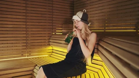Young woman drinking beverage while seated in indoor sauna at nighttime Video stock 342630581