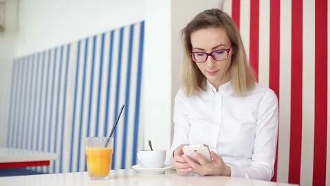 Young woman drinking coffee while browsing on mobile phone at the coffee shop Stock Footage 71780808