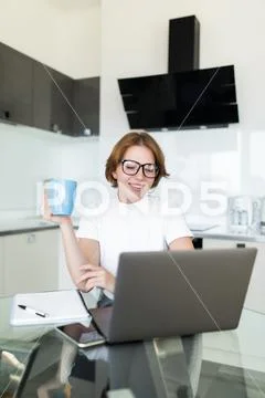 Young woman drinking coffee while on her laptop in the kitchen Stock Photos