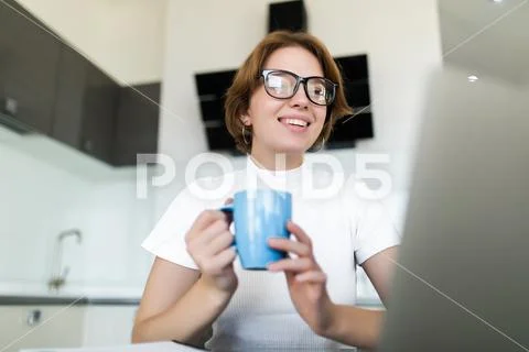 Young woman drinking coffee while on her laptop in the kitchen Stock Photos