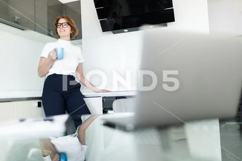 Young woman drinking coffee while on her laptop in the kitchen Stock Photos