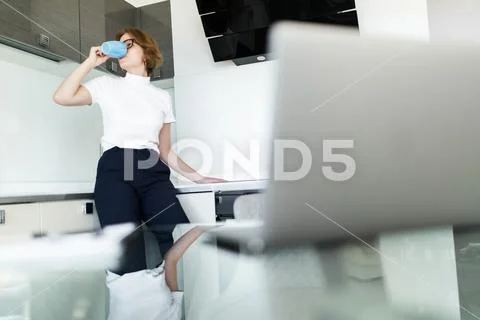 Young woman drinking coffee while on her laptop in the kitchen Stock Photos