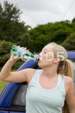 Young Woman Drinking By Electric Car