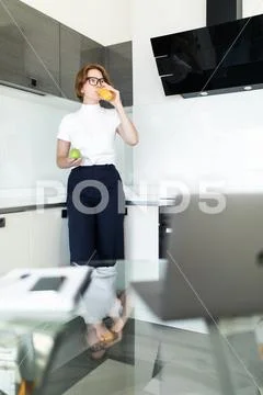 Young woman drinking juice during breakfast in kitchen Stock Photos