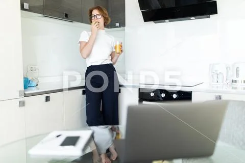 Young woman drinking juice during breakfast in kitchen Stock Photos