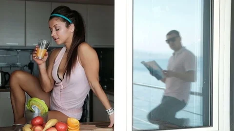 Young woman drinking juice, posing for husband in front of window Stock Footage 76138577
