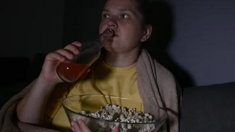 Young woman drinking kombucha while holding a large bowl of popcorn 库存影片 336900410