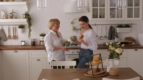 Young woman drinking tea with elderly mother at home in a modern kitchen. Stock Footage 127044997