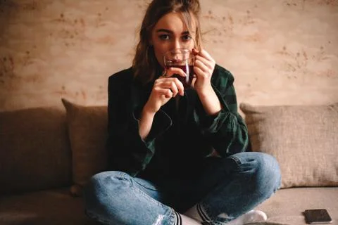 Young woman drinking tea while sitting on sofa at home Stock Photos
