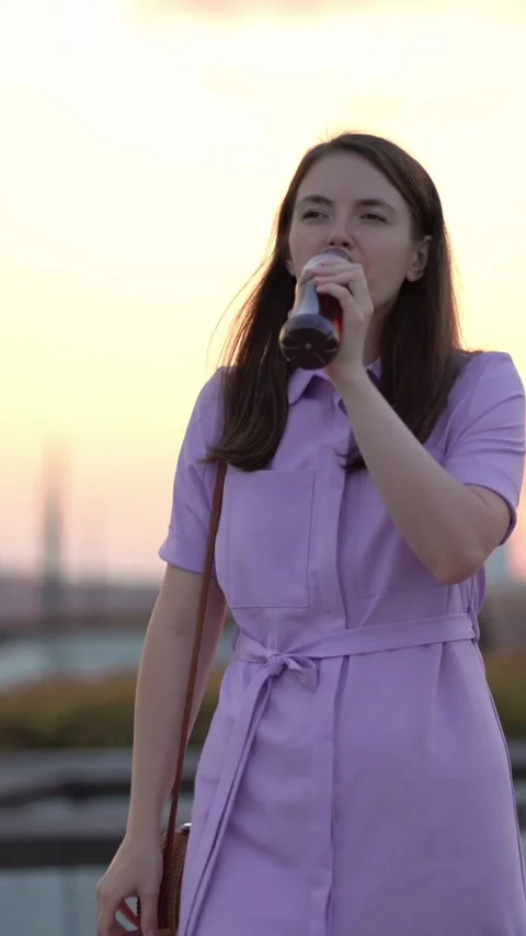 A young woman drinks refreshing cold iced tea outdoors at a beautiful sunset in Vídeos de archivo 348790145