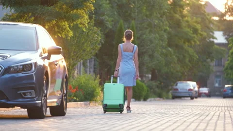 Young woman driver walking down the street pulling green suitcase. Travelling Stock Footage 158399430