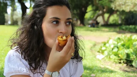 Young woman eating pastry in the park - Pastel de Nata, Belem, Lisbon Stock Footage