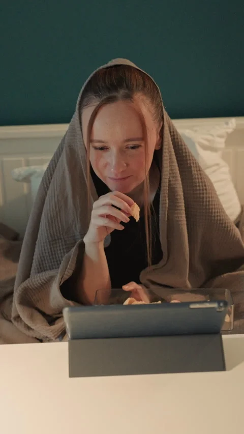 Young woman eating snacks while using tablet on bed in bedroom with teal wall Stock Footage 344429438