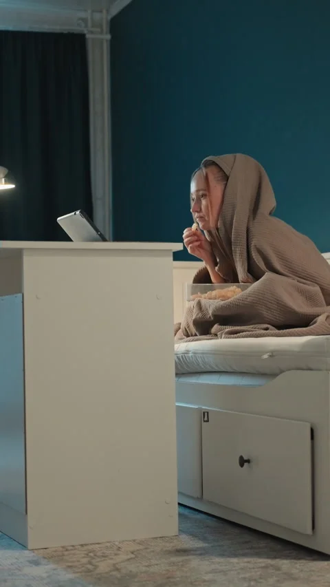 Young Woman Eating Snacks While Using Tablet in Bedroom with Teal Walls showing Stock Footage 345676244