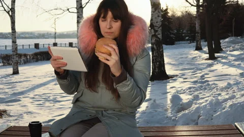 Young woman eats a burger on winter street Stock Footage 89053355