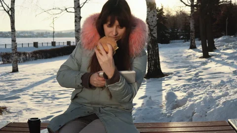 Young woman eats a burger on winter street Stock Footage 89054323