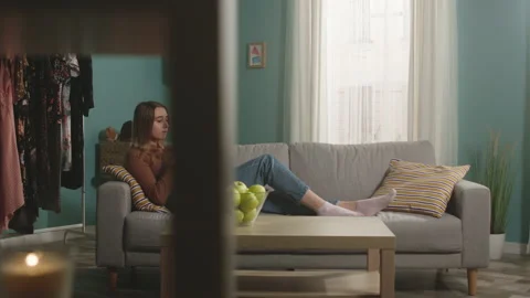 Young woman eats a red apple, lying on sofa and and watching something gadget Video stock 149146671