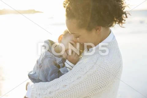 Young woman embracing daughter on beach Stock Photos