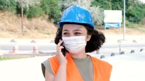 Young woman engineer or worker in facemask and helmet talking on the phone Stock Footage 137417846