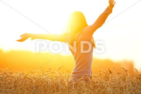 Young Woman Enjoying Sunlight With Raised Arms In Straw Field