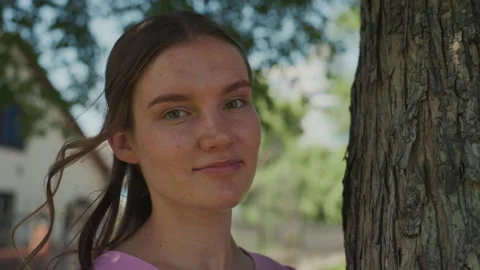 Young woman enjoying sunlight while sitting in park amidst greenery, Freckled Stock Footage 327611337