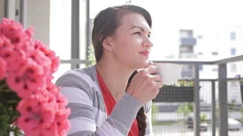 Young woman enjoys drinking coffee or tea on a balcony at home. Spring mood. Stock Footage 134171453