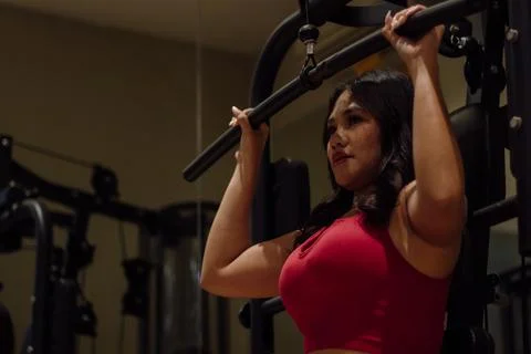 Young woman exercising on a lat pulldown machine, building upper Stock Photos