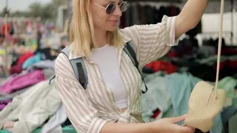 Young woman exploring handmade raffia bag at outdoor flea market, touching .. Video stock 306680635